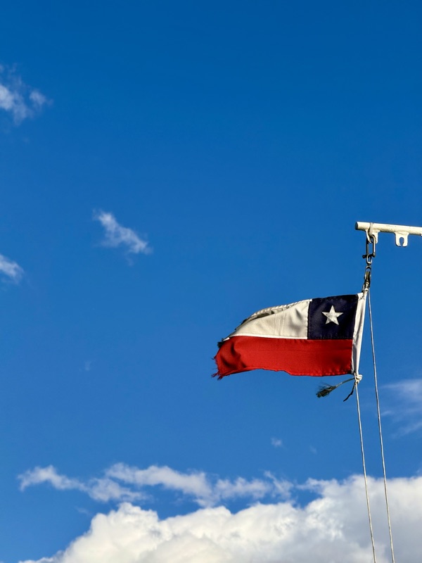 A frayed Chilean flag snapping in the wind from a white mast against a deep blue sky
