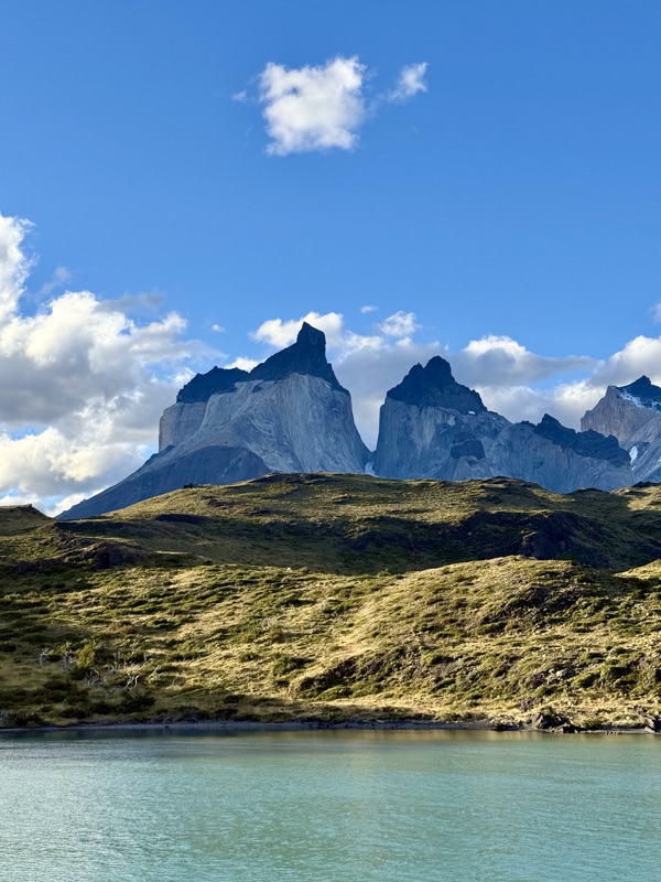 The dark-capped peaks of the Cuernos del Paine above golden grassy hills and a turquoise lake