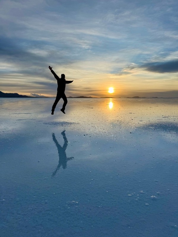 Jumping mid-air on the mirrored Salar de Uyuni at sunset, reflection below
