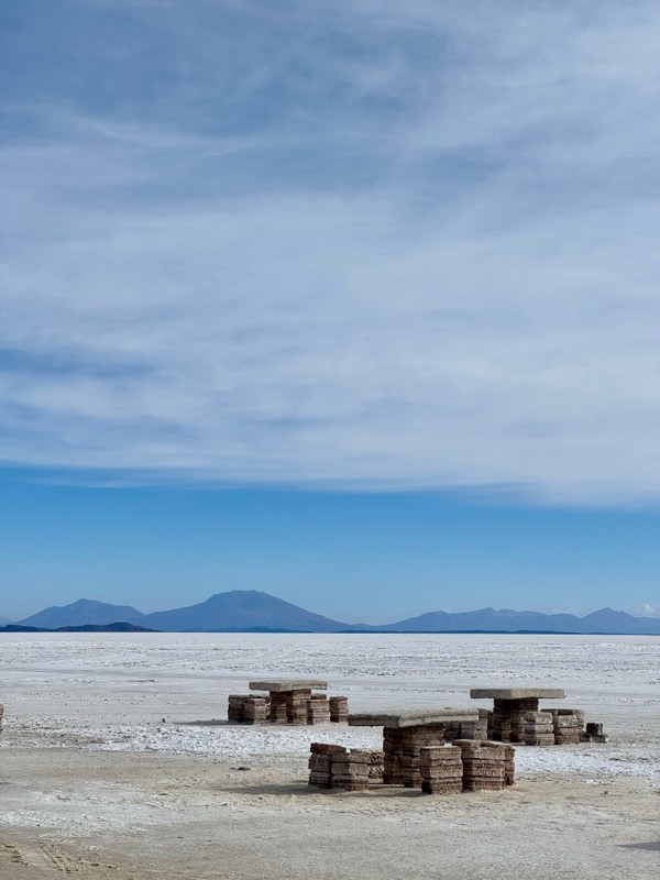 Tables built from salt bricks on the white Salar de Uyuni, distant mountains under a wide blue sky
