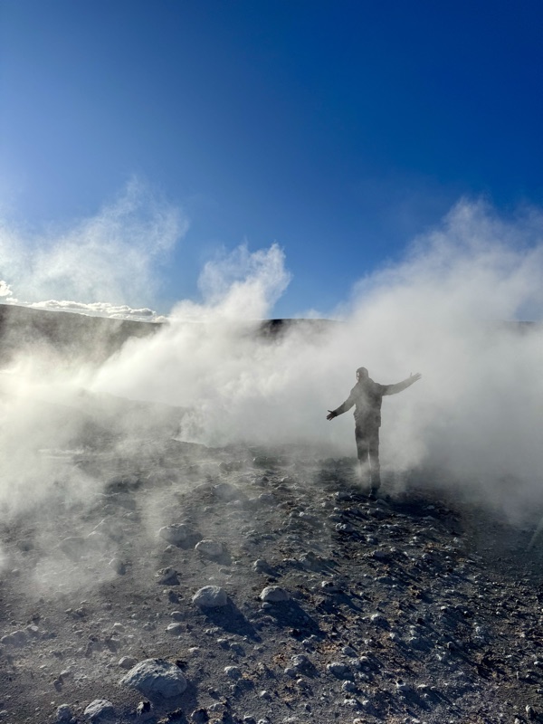 Standing with arms out in the steam of the Sol de Mañana geysers