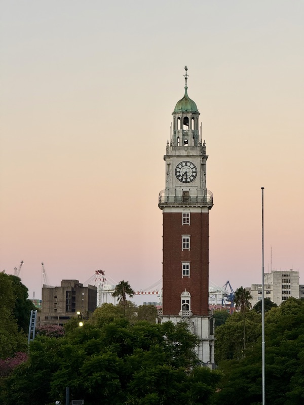 The brick clock tower of the Torre Monumental against a pink evening sky