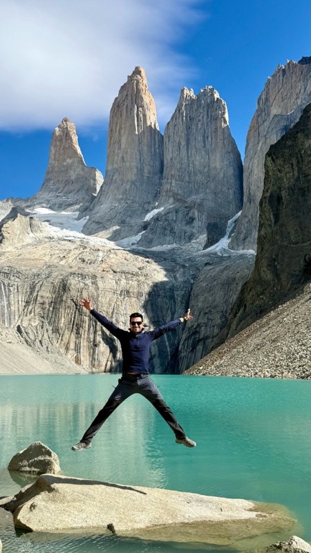 Jumping star-shaped on a rock at the turquoise lagoon below the granite towers of Torres del Paine
