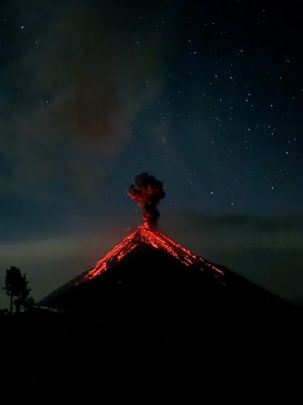Volcán de Fuego erupting at night, lava running down its flanks under the stars